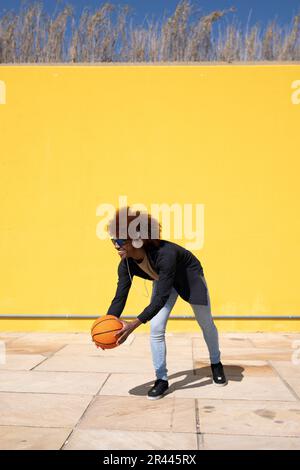 Ein junger, fröhlicher Mann, der Basketball spielt und eine Sonnenbrille trägt Stockfoto