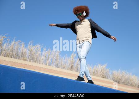 Junger glücklicher Mann mit ausgestreckten Armen balanciert an einer blauen Wand Stockfoto