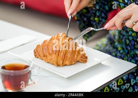 Croissant auf einem weißen Porzellanteller mit Tee auf der Seite Stockfoto