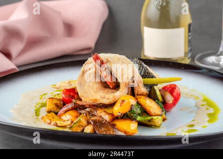 Garnelen in Wolfsbarsch eingewickelt auf verschiedenen Gemüsesorten auf einem Porzellanteller Stockfoto