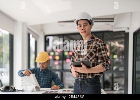 Porträt eines Ingenieurs mit Tablet im kreativen Büro. Auftragnehmer hält Tablet in architektonischen Projekten und schaut in die Kamera. Glücklicher asiate-Mann Stockfoto
