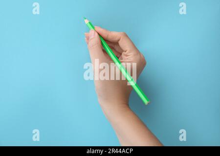 Frau mit grünem Bleistift auf hellblauem Hintergrund, Nahaufnahme Stockfoto