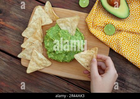 Eine Frau mit Nachos und köstlicher Guacamole aus Avocados auf einem Holztisch, Nahaufnahme Stockfoto