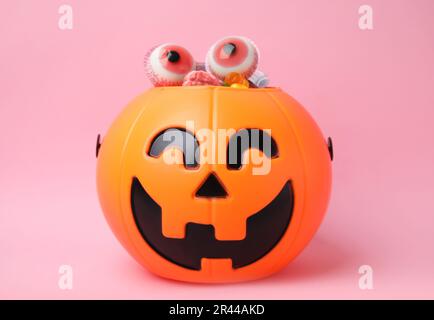 Halloween-Eimer mit verschiedenen Süßigkeiten auf pinkfarbenem Hintergrund Stockfoto