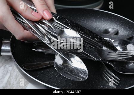 Eine Frau, die sauberes silbernes Küchengeschirr auf einem weißen Marmortisch hält, Nahaufnahme Stockfoto