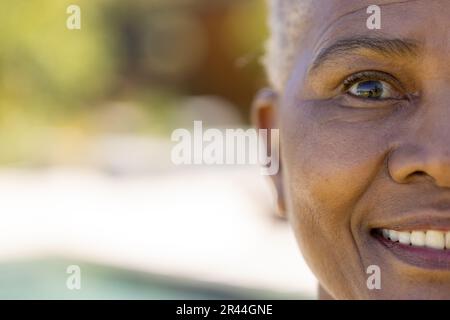 Ein halbes Porträt einer glücklichen älteren, birassischen Frau, die im sonnigen Garten lächelt, Kopierraum Stockfoto