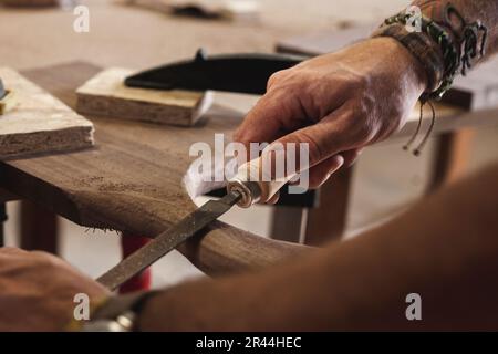 Eine Nahaufnahme der Hände eines erfahrenen Holzarbeiters, die das Holz mit einer Feile sorgfältig Formen und runden. Stockfoto
