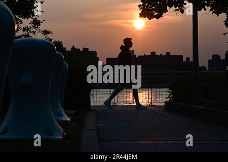 Am 23. Mai 2023 in New York City laufen die Menschen am roten Sonnenuntergang im Domino Park im Stadtviertel Williamsburg in Brooklyn vorbei. Rauch aus Canadian w Stockfoto