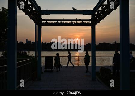 Am 23. Mai 2023 in New York City laufen die Menschen am roten Sonnenuntergang im Domino Park im Stadtviertel Williamsburg in Brooklyn vorbei. Rauch aus Canadian w Stockfoto