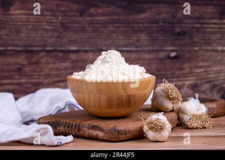 Knoblauchpulver auf Holzhintergrund. Getrocknete gemahlene Gewürze aus Knoblauchpulver in einer Holzschüssel Stockfoto