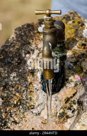 Ein Wasserhahn im Freien, der aus einem Stein kommt, mit einem Tropfen fließendem Wasser Stockfoto