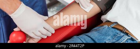 Partielle Sicht des Arztes in Latexhandschuhen, der sterilen Alkoholtupfer hält und den Wischarm des multirassischen Spenders abwischte, der vor der Blutspende in mir den Gummiball hält Stockfoto