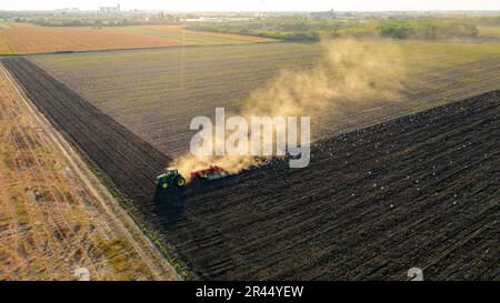 Draufsicht mit Hintergrundbeleuchtung, Zugscheibenegge, Eggen, Bodenvorbereitung für die nächste Saison, neues Erntegut. Eine Herde hungriger weißer Vögel folgt, Stockfoto