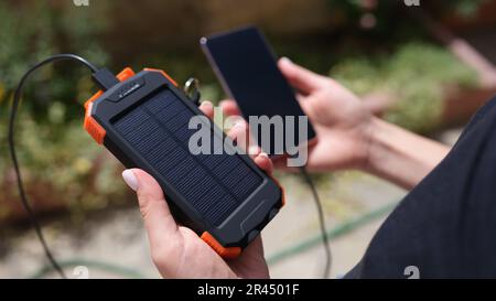 Hände halten Solarbank und Mobiltelefon zum Aufladen von Nahaufnahmen Stockfoto