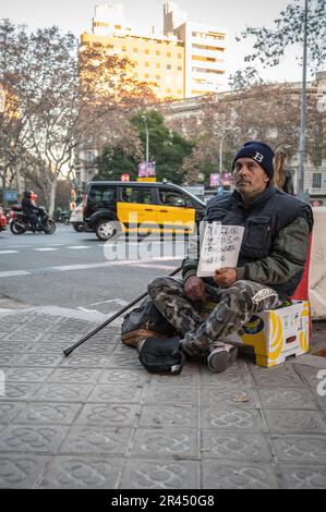 Vertikales Foto eines Bettlers, der auf einer Obstkiste sitzt und nach Geld fragt. Es ist schmutzig mit einem handgeschriebenen Schild, auf dem "Hilfe" steht Stockfoto