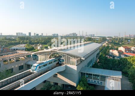Ein Blick aus der Vogelperspektive auf einen erhöhten Zug, der eine belebte Straße unter einem majestätischen städtischen Gebäude in Wuhan durchquert Stockfoto