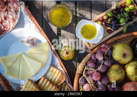 Ein hölzerner Tisch mit köstlicher mediterraner Küche einschließlich Olivenöl, Salami und Käse Stockfoto