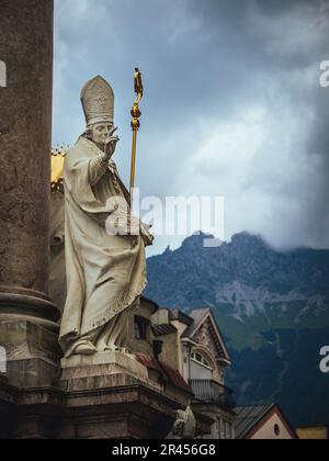 Statue des Heiligen Vigilius auf St. Annes Kolumne in Innsbruck, Tirol, Österreich, bewölktes Wetter, Sommerberge im Hintergrund Stockfoto