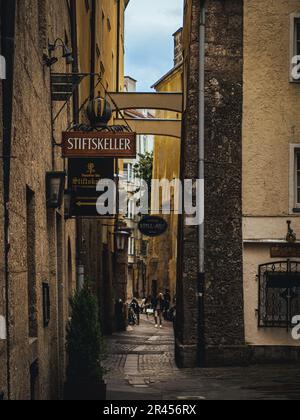 Mittelalterliche enge Gasse mit Hinweisschildern zu Gasthäusern und Menschen launisches bewölktes Wetter in Innsbruck Tirol Österreich Stockfoto