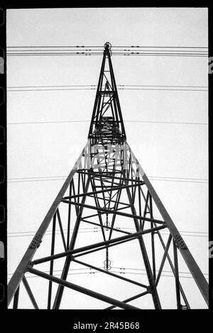 Schwarzweißfoto eines Hochspannungsmasts mit mehreren miteinander verbundenen Hochspannungsdrähten, die über den Rahmen verlaufen Stockfoto