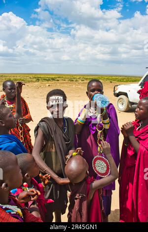 30. Dezember 2017, Serengeti-Nationalpark, Tansania-Junge Maasai-Kinder wechseln sich an einem trockenen, staubigen Tag am Eingang des Serengeti-Nationalparks ab und verdursten Stockfoto