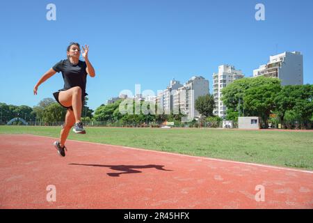 Junge argentinische, lateinamerikanische Frau in schwarzer Sportbekleidung, auf der Laufbahn mit langen Sprüngen, Kopierraum, Sportkonzept. Stockfoto