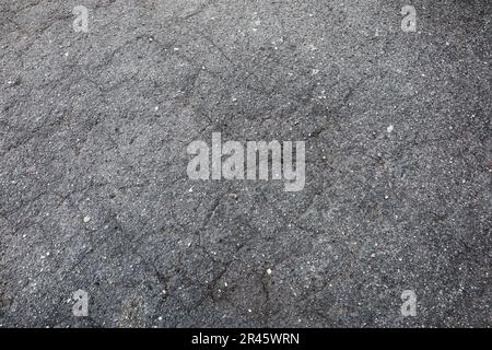 Abgebrochene graue Asphaltstraße, die Risse aufweist. Auf den schwarzen Linien auf der Straße sind Kies. Nahaufnahme von Transport- und Bauarbeiten Stockfoto