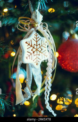 Nahaufnahme eines festlichen Sternspielzeugs, das an einem Weihnachtsbaum hängt und von Bokeh-Lichtern beleuchtet wird Stockfoto