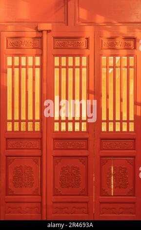 Das gelbe Licht geht durch die rote traditionelle chinesische Holztür mit geschnitzten Blumen. Stockfoto