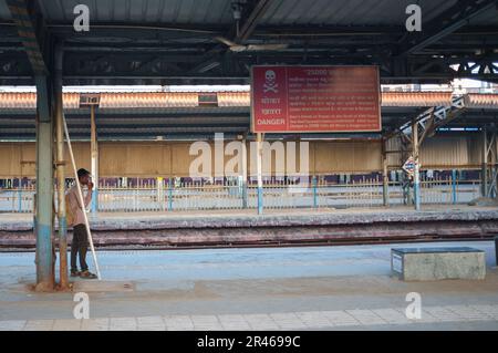 Ein Mann auf einem Bahnsteig unter einem Gefahrenschild in Mumbai Stockfoto