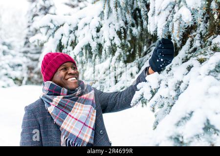 afroamerikanischer Handsom-Mann in rotem Hut und stilvollem karierten Mantel Blick auf die Kamera mit toothy schneeweißen Lächeln im Freien im Park Stockfoto