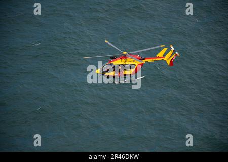 Ein leuchtend gelber Hubschrauber mit einer Person im Cockpit, die über einem ruhigen Gewässer schwebt Stockfoto