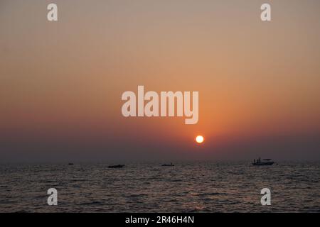 Ein atemberaubender Blick aus der Vogelperspektive auf den Sonnenuntergang über dem Horizont des riesigen Ozeans, mit einem Pier, der sich im Vordergrund bis ins Meer erstreckt Stockfoto