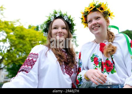 Zwei junge ukrainische Frauen, die im Wind tanzen, entwickeln Haare und Blumen in der Nähe des Kranzes auf Köpfen wunderschöne bestickte Hemden Zeitlupe junge Mädchen, die vor den Bäumen und dem Himmel tanzen Stockfoto