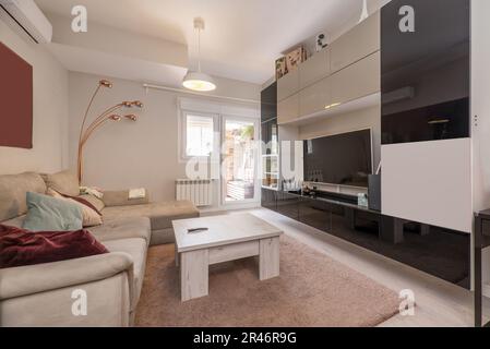 Wohnzimmer mit Bücherregal, das eine Wand bedeckt, mit einem großen Fernseher in der Mitte und einem grauen Stoffsofa mit Chaiselongue Stockfoto