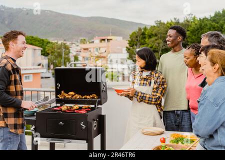 Glückliche, generationenübergreifende Menschen, die Spaß beim Grillen auf dem Dach des Hauses haben - Sommerversammlungen und Essenskonzept Stockfoto