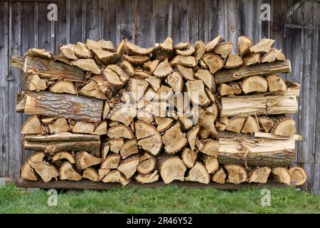 Rustikaler Holzstapel im Gras vor der Holzwand einer Scheune Stockfoto