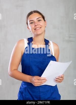 Glückliche Arbeiterin in Arbeitskleidung, die steht und Papiere hält Stockfoto