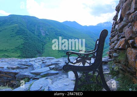 Eine schwarze Holzbank auf einem felsigen Berg mit Blick auf ein wunderschönes Tal darunter Stockfoto
