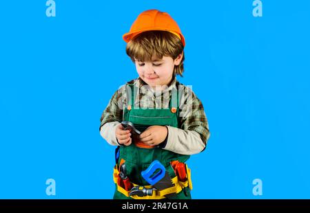 Kleiner Junge im Schutzhelm und Werkzeuggürtel mit Rohrzange. Kind in Bauernuniform mit verstellbarem Schraubenschlüssel. Reparaturwerkzeug. Kleiner Mechaniker Stockfoto
