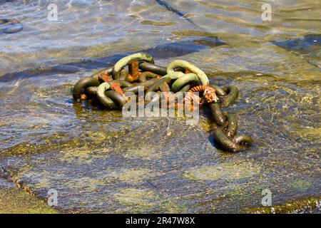 Eine Nahaufnahme einer veralteten Metallankerkette, die an eine größere Kette geklebt ist, die im Ozean untergetaucht ist Stockfoto