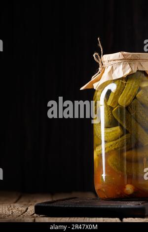 Eingelegte Gurken in einem geschlossenen Glasgefäß auf einer Holzunterlage mit Platz für Text. Hausgemachte Gurken in Dosen in einem Glas Stockfoto