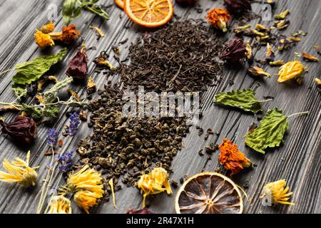 Zusammensetzung von trockenem schwarzem und grünem Tee, getrockneten Zitrusscheiben, Minzblättern und trockenem Hibiskus, Kalendula, Lavendelblüten auf dunklem Holzhintergrund Stockfoto