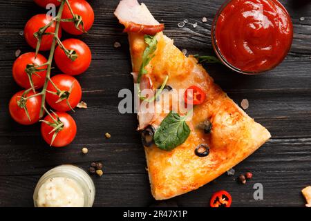 Ein Stück Pizza mit Fleisch, Saucen und frischen Kirschtomaten auf dunklem Holzhintergrund, Draufsicht. Stockfoto