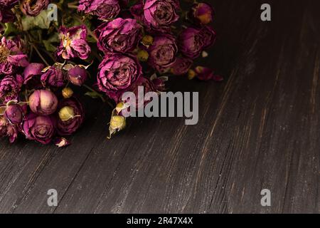 Strauß trockener rosafarbener Rosen auf dunklem Holzhintergrund, Nahaufnahme. Begriff der Einsamkeit oder des Alters. Traurigkeit, unglückliche Liebe. Stockfoto