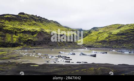 Ein malerischer See, umgeben von üppig grünen Bergen mit ein paar kleinen Eisschollen, die auf der Oberfläche in Island treiben Stockfoto