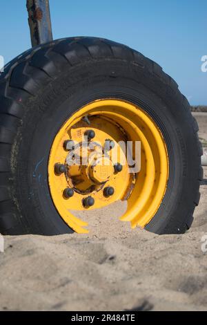 Großes gelbes Rad von einem Bootsanhänger am Strand Stockfoto