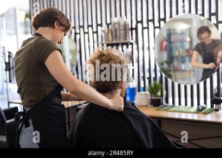 Eine weiße Friseurin, die männlichen Kunden einen Umhang anzieht, bevor sie im Friseursalon arbeiten Stockfoto