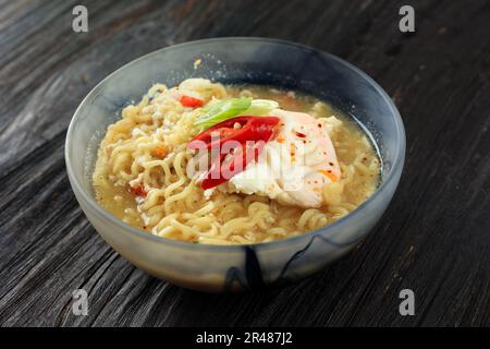 Scharfe Instant-Nudelsuppe mit pochiertem Ei, grünen Zwiebeln und Chili. Indomie Rebus Stockfoto