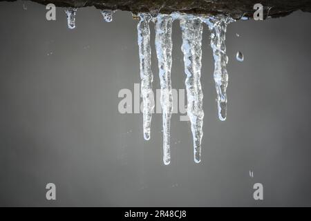 Ein Eiszapfen hängt an einem Industrierohr an der Seite eines Gebäudes Stockfoto